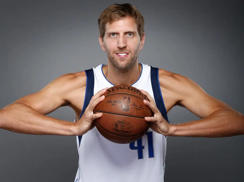 Professional basketball player in a Dallas uniform holding a basketball for a studio portrait.