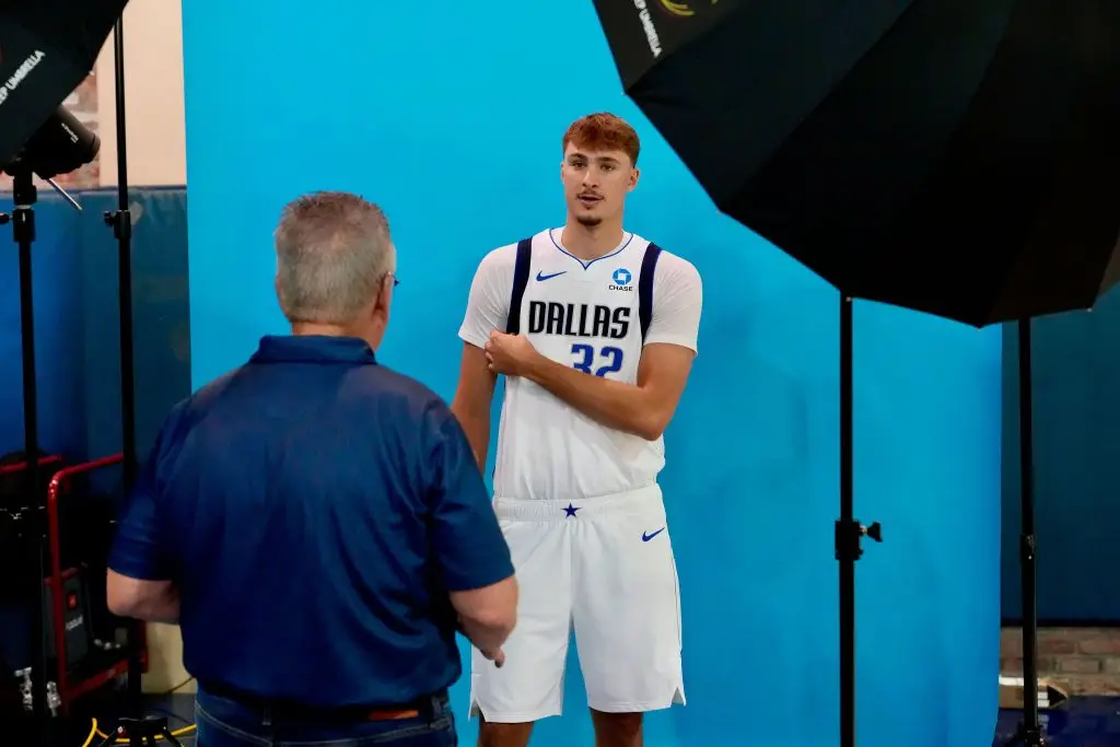 Photographer giving direction to a player in a white number 32 Dallas jersey in front of a blue backdrop