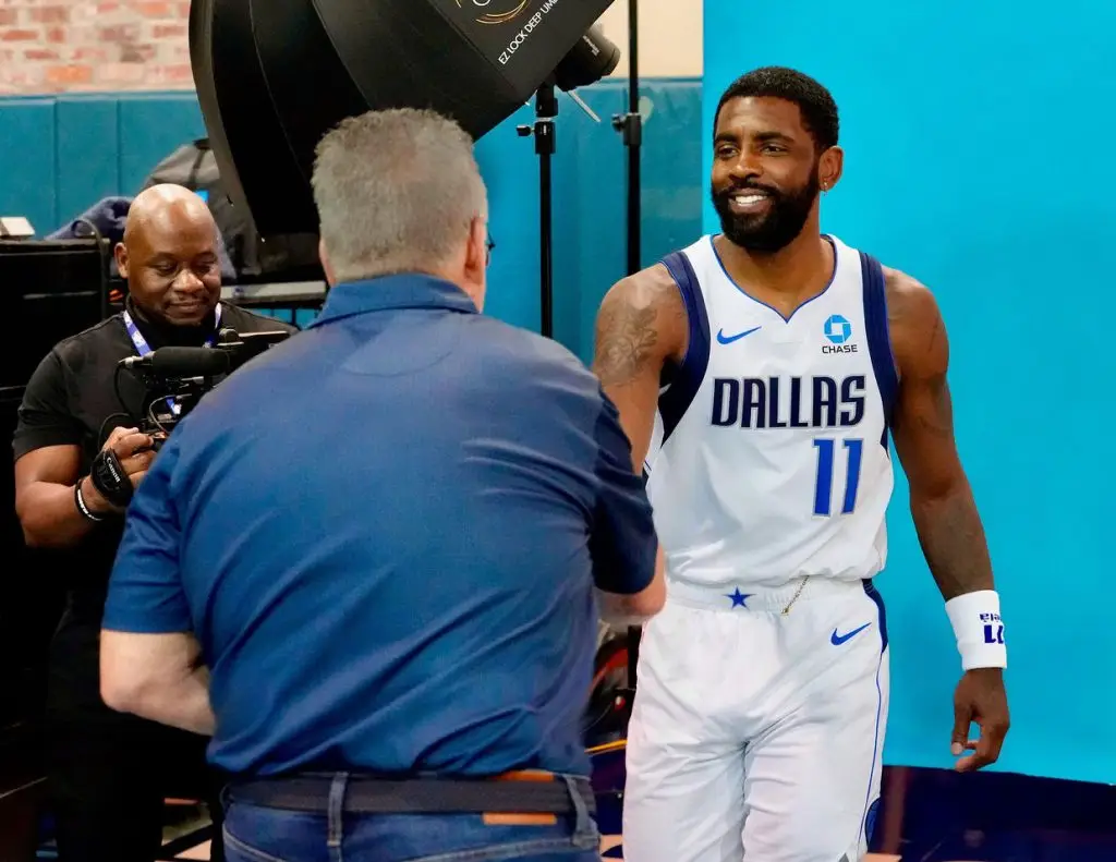 Photographer shaking hands with a smiling player in a white number 11 Dallas jersey while a videographer films in the background