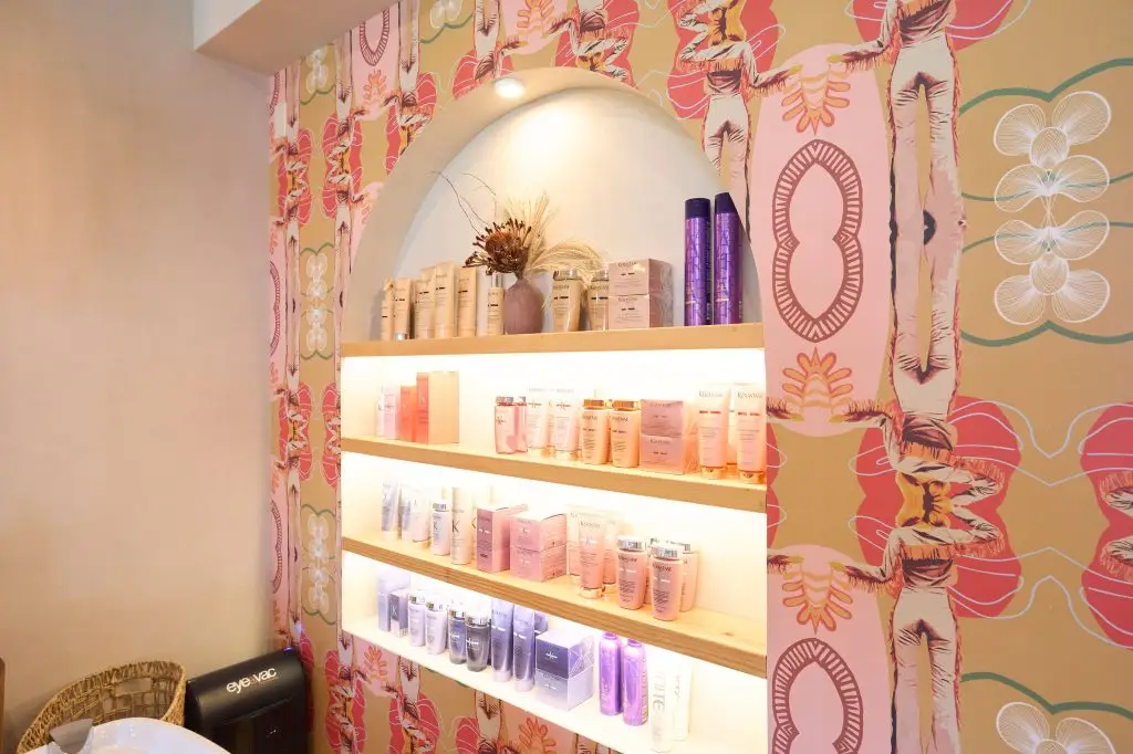 Shelves of hair care products displayed in an arched alcove against patterned wallpaper